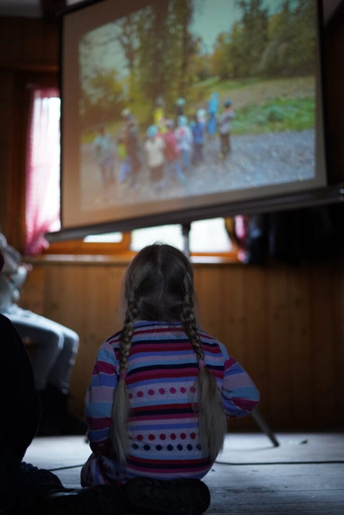 Das Bild zeigt eine kleine Pfadfinderin, die sich auf den Knien sitzend eine Diashow während der Adventsfeier ansieht.