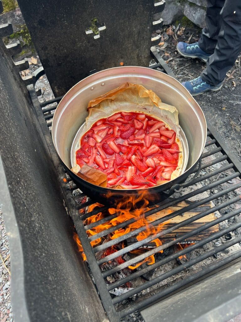 Das Bild zeigt eine Erdbeer-Wähe, die auf einem Holzkohlegrill gebacken wird.