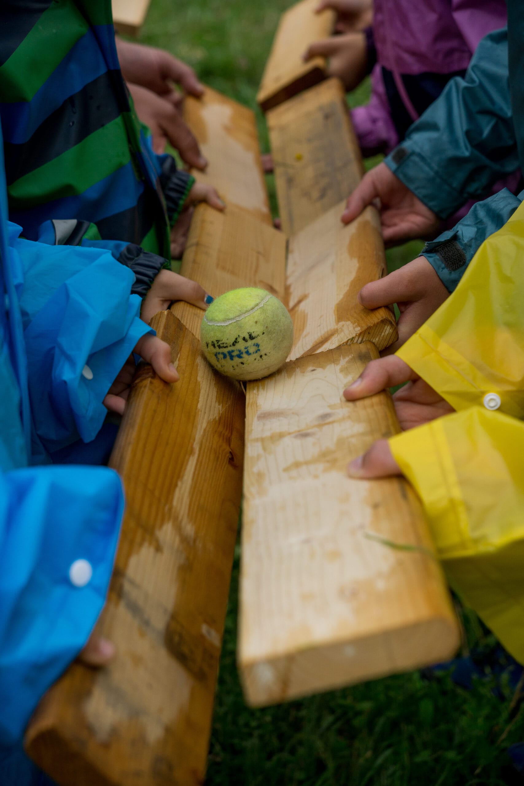 Das Bild zeigt, wie ein paar Pfadfinder ein Spiel spielen, bei dem ein Tennisball durch in die Luft gehaltene Holzbretter, die eine Bahn bilden, eine bestimmte Strecke zurücklegen muss.