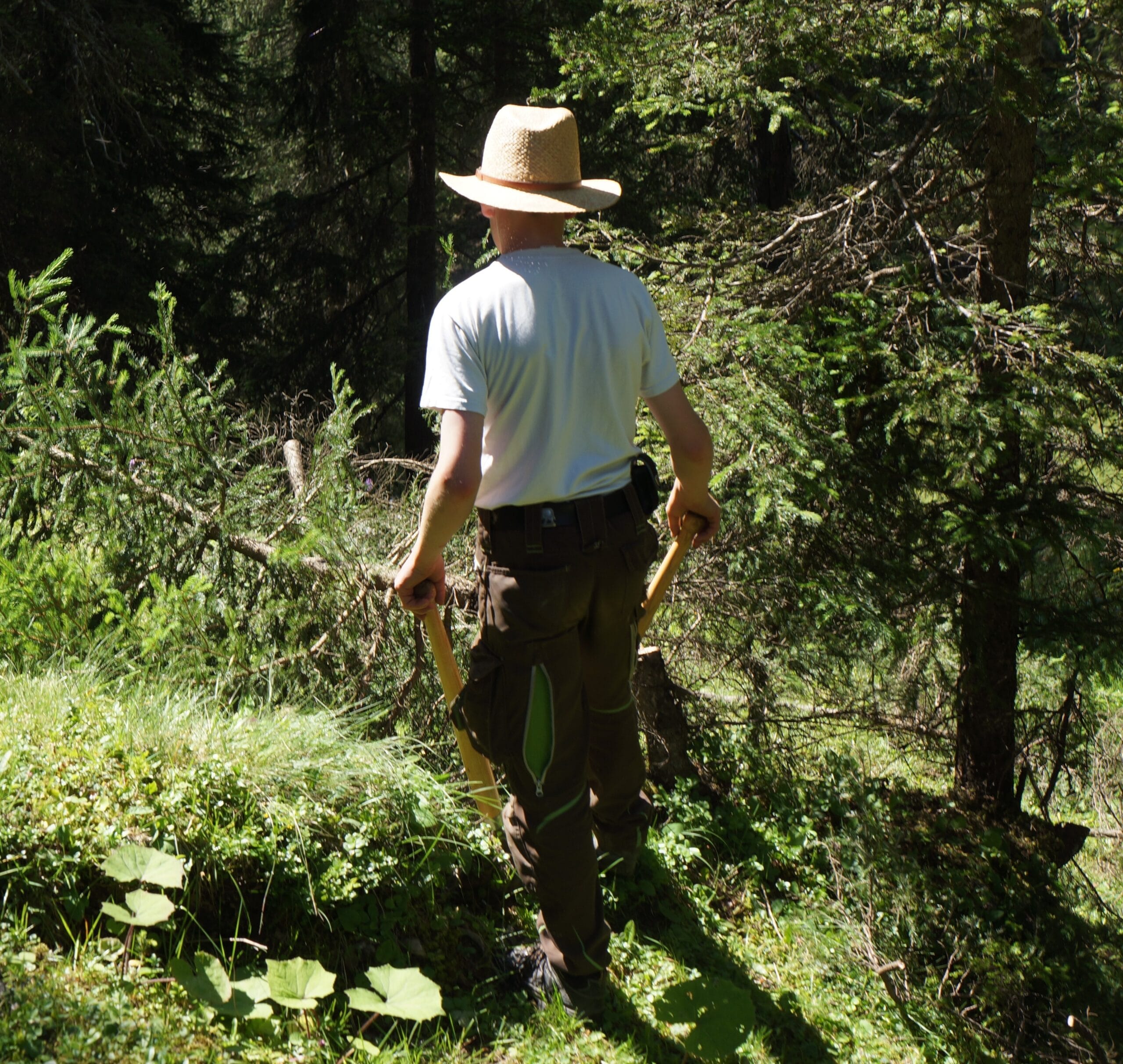Das Bild zeigt einen junen Pfadfinder, der einen auffälligen Strohhut trägt und im Wald arbeitet.