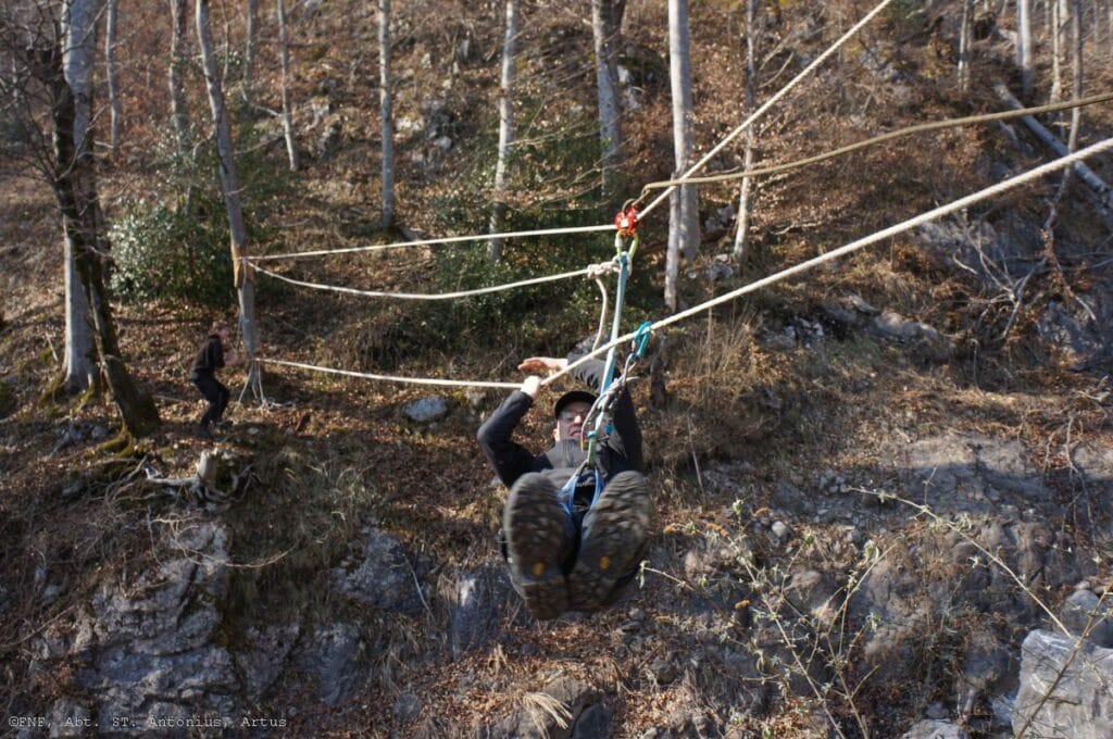 Dieses Bild zeigt einen Pfadfinder, der mit einer Sicherung an einem Seil hängend über eine Schlucht hinwegfegt.