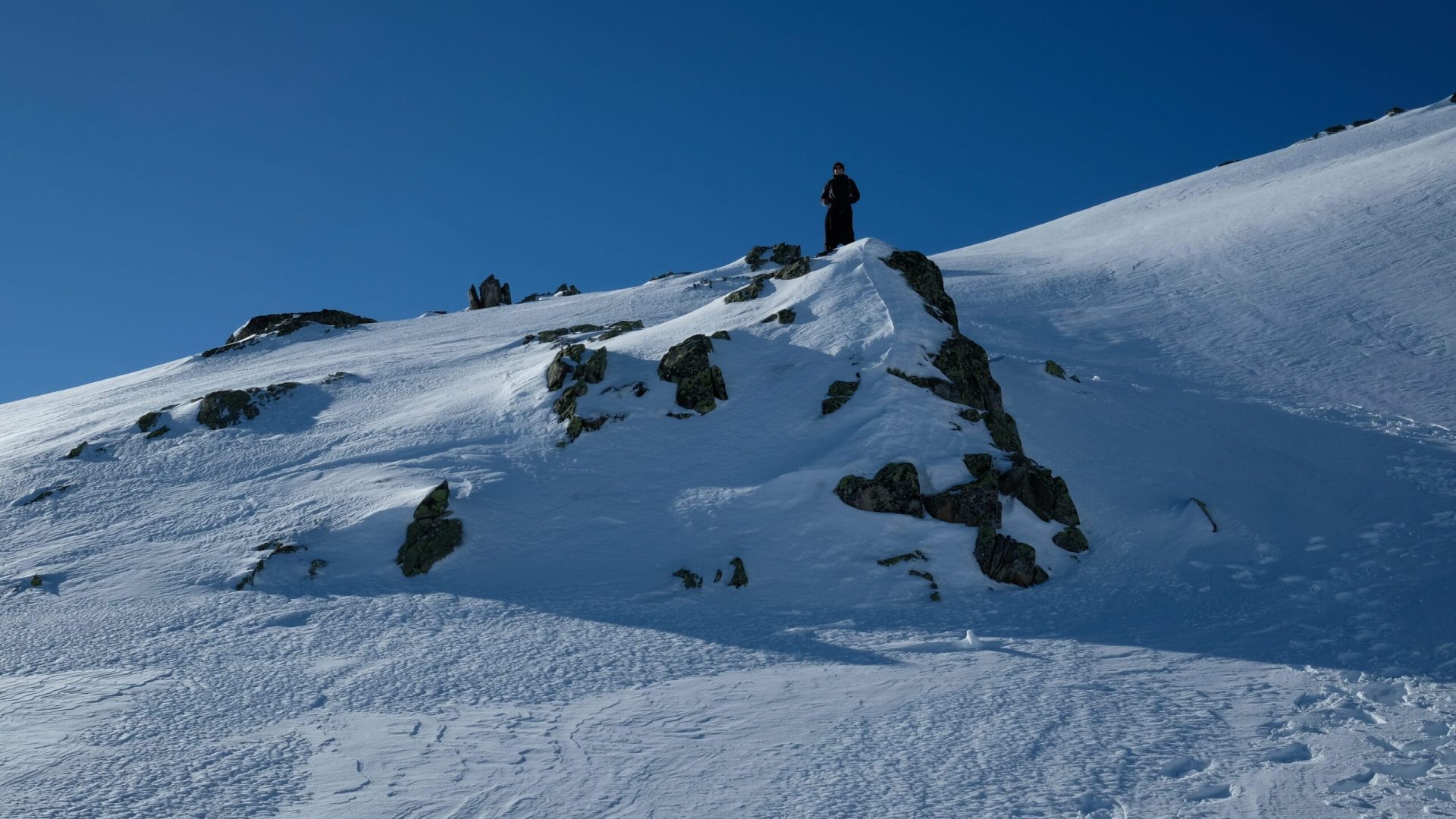 Das Bild zeigt einen Priester, der auf einem mit Schnee bedecktem Berg steht.