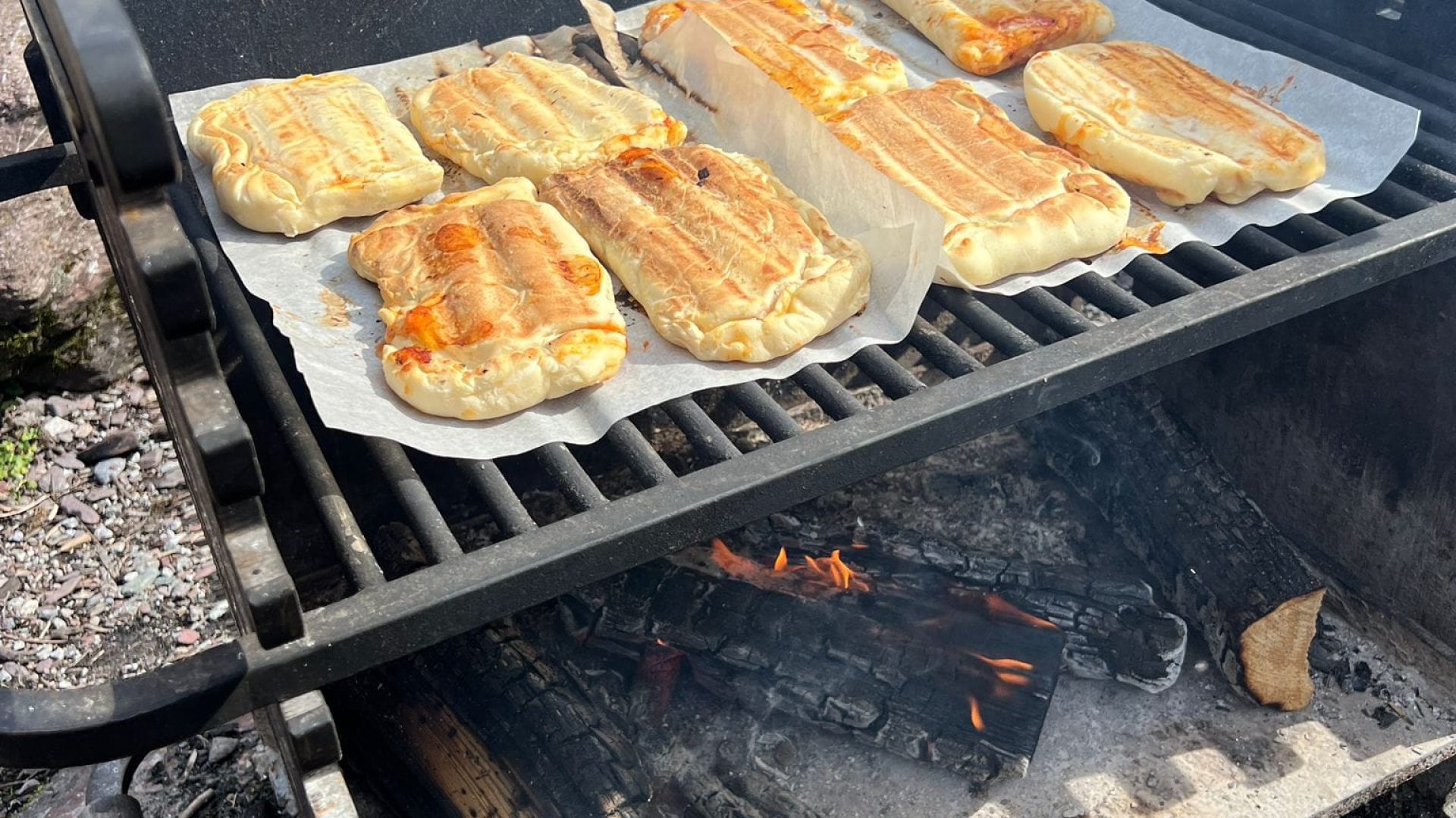 Das Bild zeigt einen Holzkohlegrill, auf dem gerade selbstgemachte Calzone-Pizzen gebacken werden.